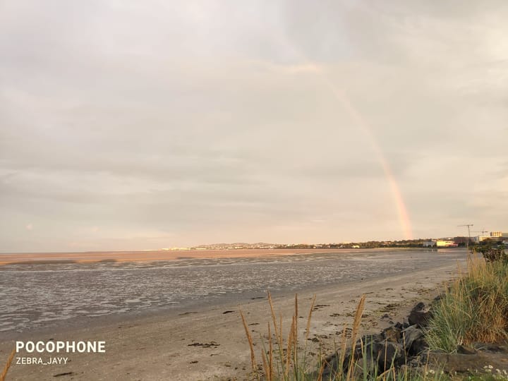 A picture of a shore there's a faint rainbow in the back